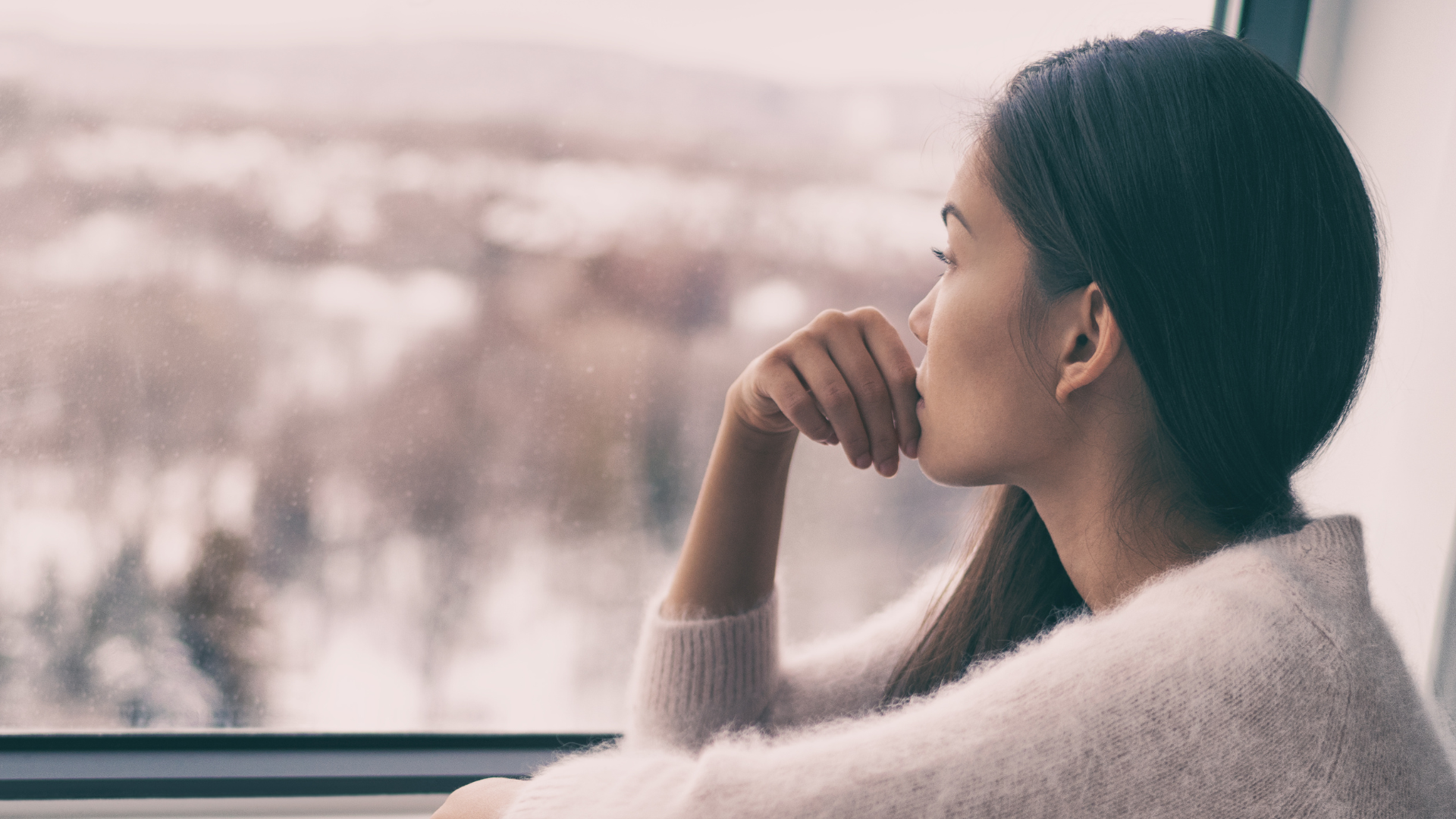 A woman peers out her window despondently.