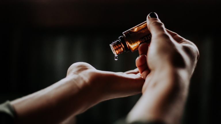 A set of hands puts drops essential oil into their palms.