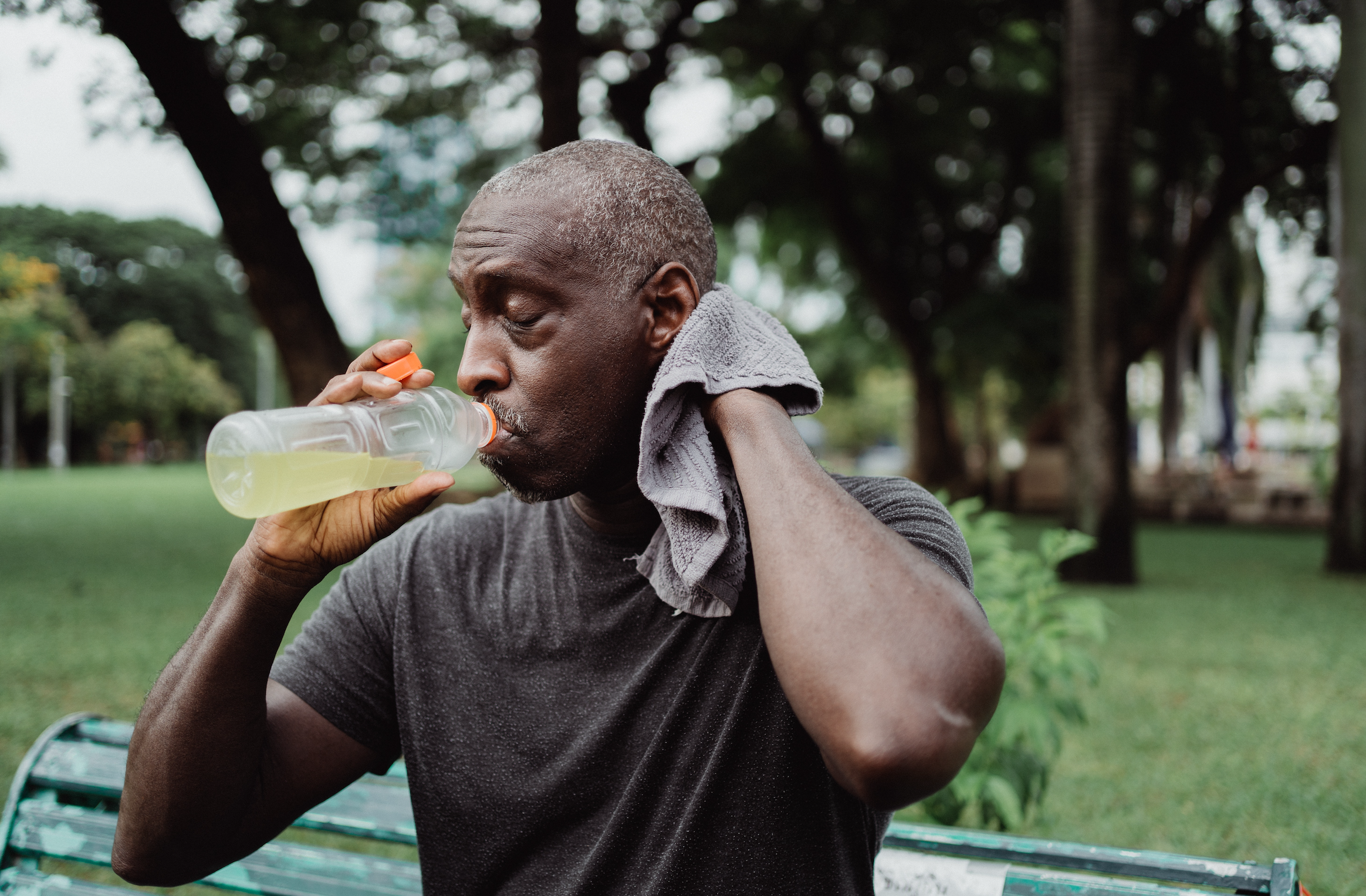 A man wipes sweat from his neck while sipping a sports drink.