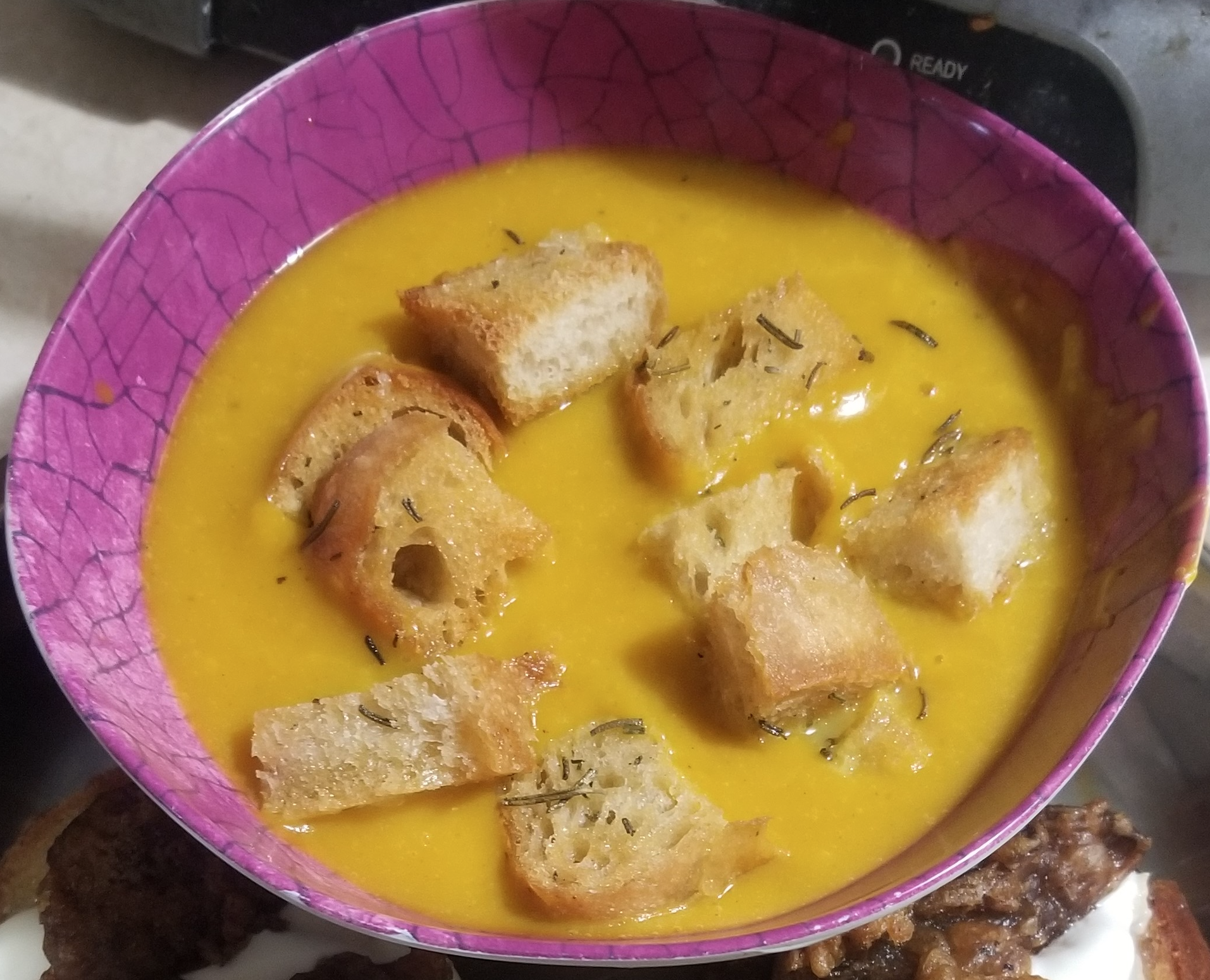 Pink bowl holding a vibrant gold colored soup topped with croutons.