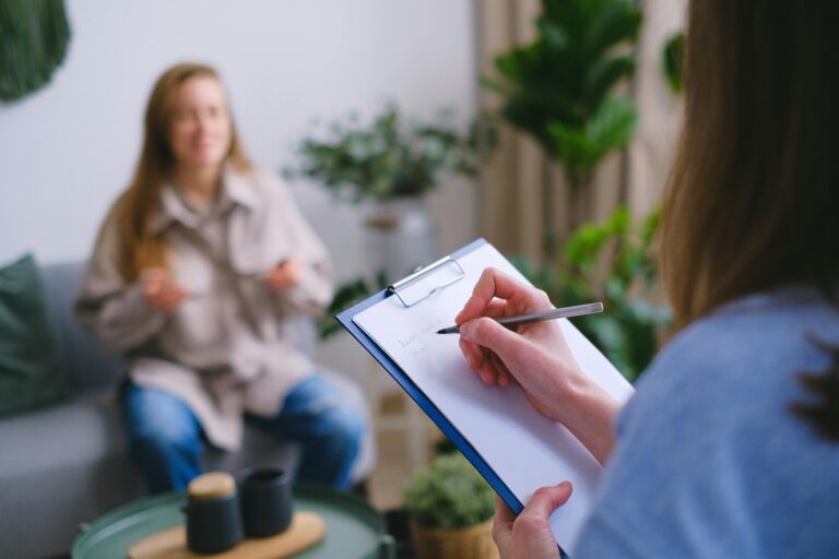 A patient talks while a health care provider takes notes on a clipboard.