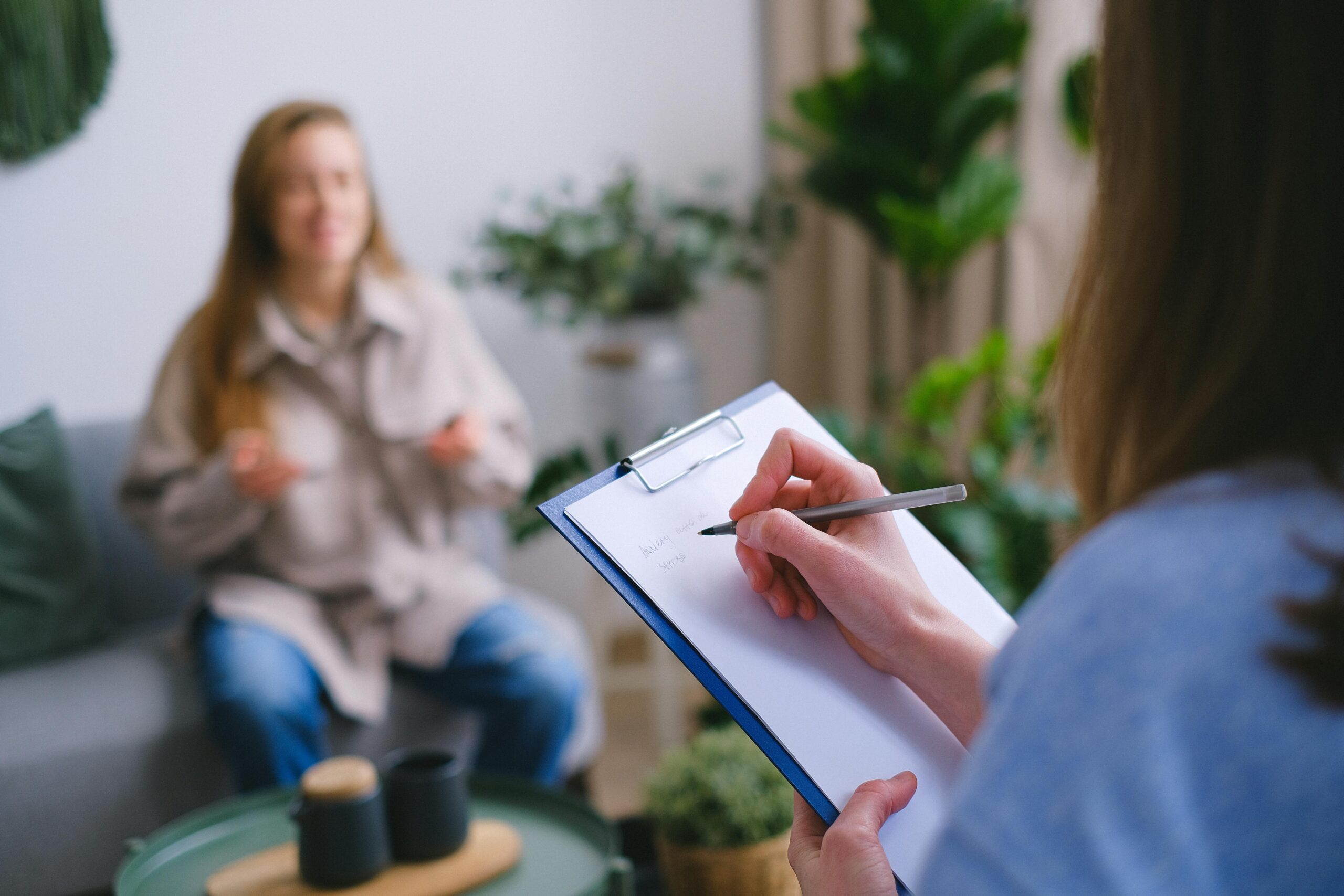 A patient talks while a health care provider takes notes on a clipboard.